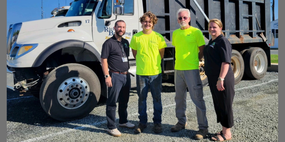 four adults standing by dump truck